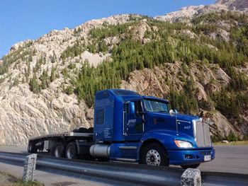 Blue Kenworth flatbed parked in front of a mountain