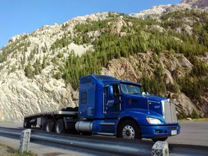 Blue Kenworth tractor trailer parked in front of a mountain